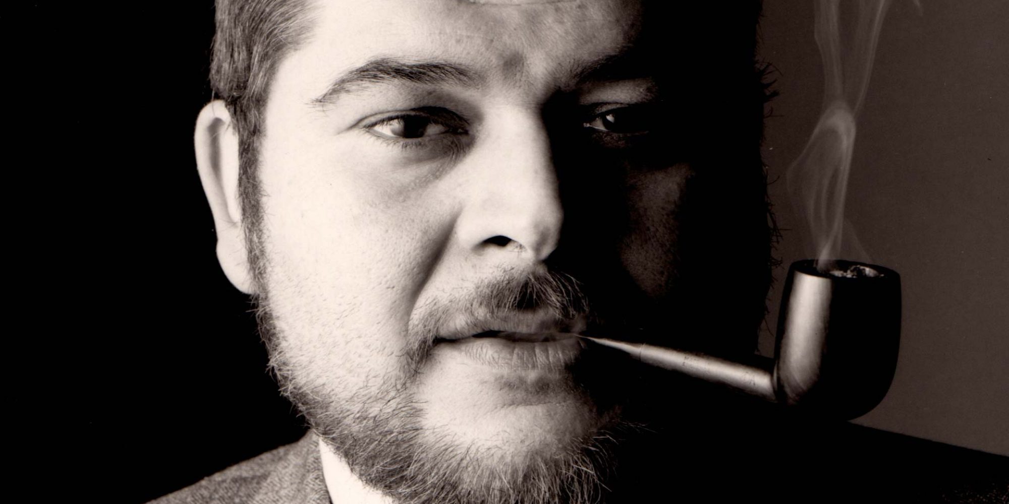 Black and white photograph close up of Joe Colombo's face. He is smoking a pipe.