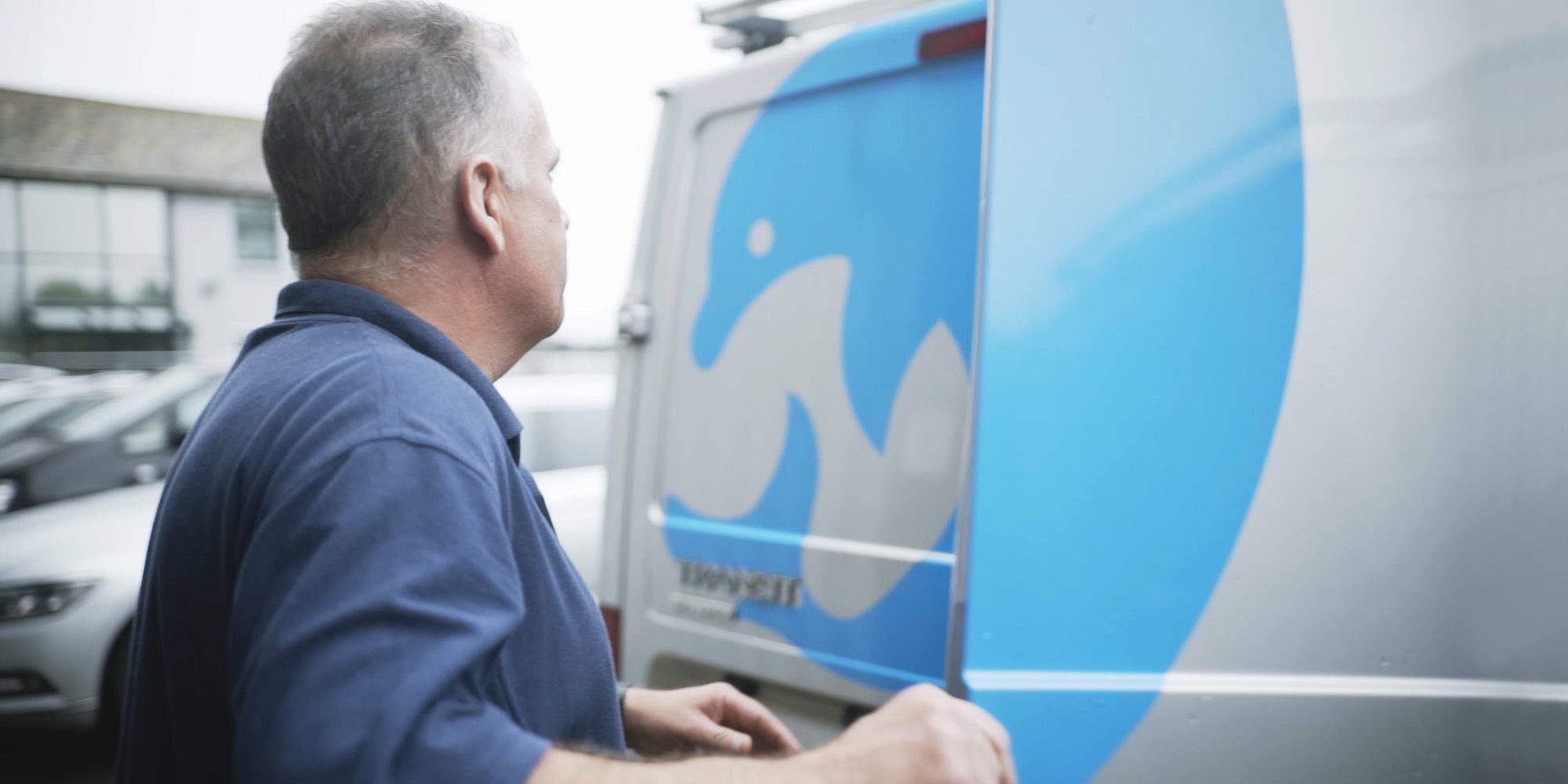 Man closing van back door. The door has a blue dolphin graphic printed on it.